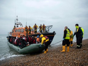 Migrants are helped ashore from a Royal National Lifeboat Institution lifeboat at a beach in Dungeness, on the south-east coast of England, on November 24, 2021, after being rescued while crossing the English Channel.