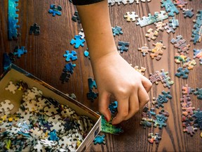A youth's hand collects and assembles puzzle pieces of a jigsaw on a wooden background. background selective blur, concept