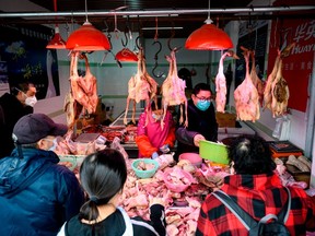 People wearing protective face masks shop at a chicken stall at a wet market in Shanghai on February 13, 2020.