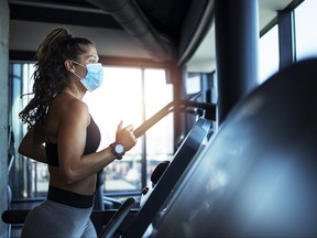 Sportswoman training on treadmill in gym and wearing face mask to protect herself against coronavirus during global pandemic of covid-19 virus.