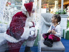 Three-year-old Rinayah chats with Santa Claus through a solid plexiglass barrier at White Oaks Mall in London, Ont. on Friday December 18, 2020.