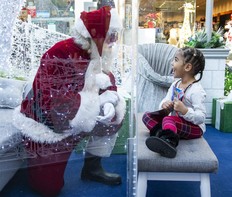 Three-year-old Rinayah chats with Santa Claus through a solid plexiglass barrier at White Oaks Mall in London, Ont. on Friday December 18, 2020.