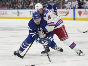Maple Leafs forward Auston Matthews (34) and Rangers forward Greg McKegg (14) battle for the puck during NHL action at Scotiabank Arena in Toronto, Oct. 18, 2021.