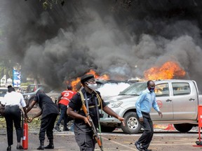People extinguish fire on cars caused by a bomb explosion near Parliament building in Kampala, Uganda, Tuesday, Nov. 16, 2021.