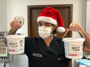 Dr. Giancarlo McEvenue, a plastic surgeon who performed female-to-male chest surgeries at McLean Clinic in Mississauga, holds two medical waste buckets labelled "breast tissue" while dressed in a Santa hat in a photo that was posted on social media.