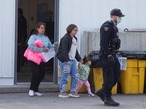 Asylum seekers follow a RCMP officer after being processed for crossing the border from New York into Canada, at Roxham Road, in Hemmingford, Que., March 19, 2020.