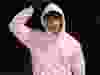 Man in pink hoodie touching hood with right hand.