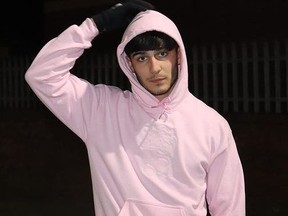 Man in pink hoodie touching hood with right hand.