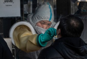 A medical worker reaches through protective gloves as she administers a nucleic acid test to a client at a private outdoor clinic on December 27, 2021 in Beijing, China. (Kevin Frayer/Getty Images)