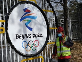 A mask-wearing construction worker walks past the Beijing 2022 Winter Olympic Games logo on a street in Beijing on Dec. 11, 2021.
