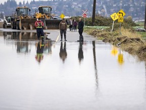 People watch the rising flood waters coming from the United States into Huntington Village in Abbotsford, B.C., Monday, November 29, 2021.