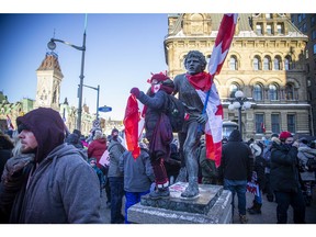 A protester stands on the Terry Fox statue that was outfitted with Canada flags and earlier had signage stuck to it.