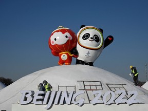 Workers set up an installation displaying the mascots of the Beijing 2022 Winter Olympic and Paralympic Games, along a street in Beijing on January 11, 2022.