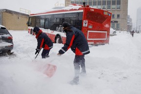 Toronto Transit Commission workers try to clear a roadway as a bus sits stuck since the morning hours in Toronto after a major blizzard dumped as much as 60 cm of snow on parts of Southern Ontario, closing major highways and roadways, in Toronto, Jan. 17, 2022.