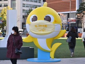 People walk past a shark character from the children's song "Baby Shark" at Seoul Plaza in Seoul on November 3, 2020.