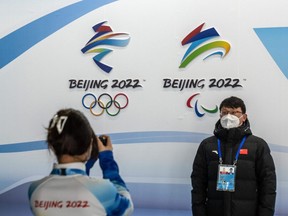 A man has his picture taken next to Winter Olympics and Paralympics branding at the Main Press Centre in Beijing, China, Wednesday, Jan. 26, 2022.