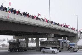 Supporters holding Canadian flags stand on an overpass and cheer as trucks pass by while honking their horns as they travel on Highway 400 in Toronto on Thursday Jan. 27, 2022.