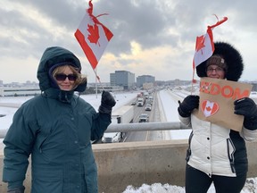Die Unterstützer von Freedom Convoy, Fran Boudrie (L) und Mary Fenwick (R), halten kanadische Flaggen, während sie auf einem Highway stehen.  Überführung 401 an der Mississauga Rd.