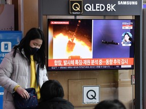 A woman stands in front of a television screen showing a news broadcast with file footage of a North Korean missile test, at a railway station in Seoul on January 27, 2022.