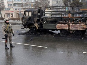 A Kazakh law enforcement officer stands guard near a burnt truck while checking vehicles following mass protests triggered by a fuel price increase, in Almaty, Kazakhstan, Saturday, Jan. 8, 2022.