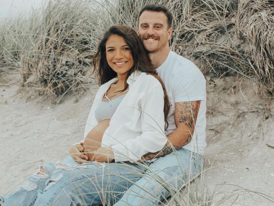 Young couple expecting first child smiling, sitting on a beach.