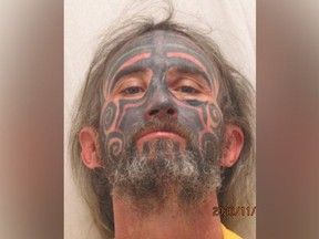 Mugshot of man with unruly hair and a tattoo covering his entire face.