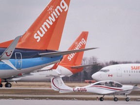 A small plane taxis past Boeing 737s belonging to Canadian Vacation air carrier Sunwing sit on the tarmac at Waterloo International Airport in Waterloo, Ont., March 24, 2020.