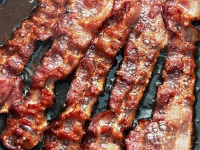 Bacon slices are cooked in a pan.