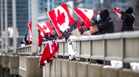 Unterstützer von Lkw-Fahrern schwenken Flaggen in Richtung der Fahrspuren in Richtung Osten auf dem Highway.  401, von der Don Mills Rd.  Überführung, in Toronto, Ontario.  am Donnerstag, 27. Januar 2022.