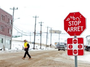 A man wearing a mask to help slow the spread of coronavirus disease (COVID-19) passes a stop sign written in English, French and Inuktitut as the territory of Nunavut enters a two week mandatory restriction period in Iqaluit, Nunavut, Canada November 18, 2020.