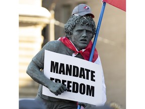 A statue of Terry Fox is adorned with a Canadian flag, protest sign and hat as protesters participating in a cross-country truck convoy gather on Parliament Hill in Ottawa on Saturday, Jan. 29, 2022.