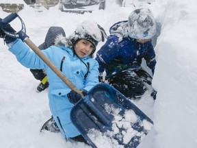 Children help to clear snow from a driveway on Monday, January 17, 2022, in Ajax.