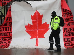 A security guard walks in front of a Canadian flag during the Freedom Convoy demonstration in front of Parliament Hill on Wellington St. in Ottawa, Feb. 9, 2022.