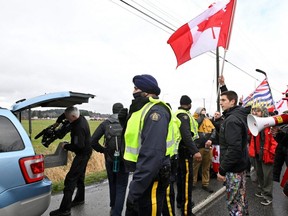 RCMP officers help a cameraman from Global News access his vehicle as a convoy of vehicles and supporters gathered near the border as they continue to protest against COVID-19 vaccine mandates, in Surrey, B.C., Saturday, Feb. 19, 2022.