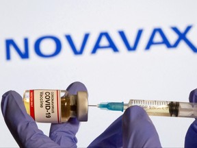 A woman holds a small bottle labeled with a "Coronavirus COVID-19 Vaccine" sticker and a medical syringe in front of displayed Novavax logo in this illustration taken, Oct. 30, 2020.