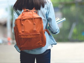 Back of university student with backpack while going to college by walking from street, teenager in campus, education concept