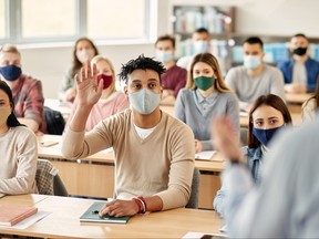 Black student raising his hand to answer a question while attending lecture in the classroom during COVID-19 pandemic.