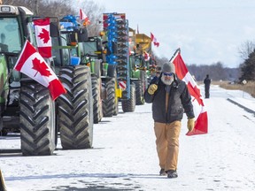 A man paces up and down the line of 18 farm vehicles parked on Highway 402 at the Forest Road exit in Lambton County, Ont. on Sunday February 13, 2022. On Thursday, there were 20 vehicles. The Ontario Provincial Police have closed the westbound lanes of Highway 402 between Nauvoo Road and Forest Road. I(Derek Ruttan/The London Free Press)