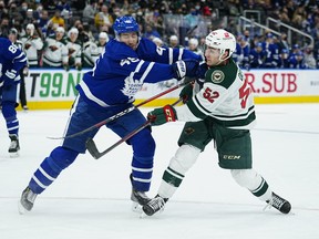 Minnesota Wild's Connor Dewar (right) shoots the puck as he is hit by Maple Leafs' Ilya Lyubushkin during the second period at Scotiabank Arena on Thursday, Feb. 24, 2022.