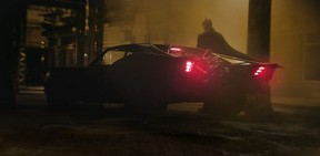 Robert Pattinson as Batman with the Batmobile in a scene from The Batman.