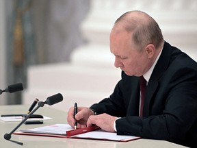 Russian President Vladimir Putin signs documents, including a decree recognising two Russian-backed breakaway regions in eastern Ukraine as independent entities, during a ceremony in Moscow, in this picture released February 21, 2022.