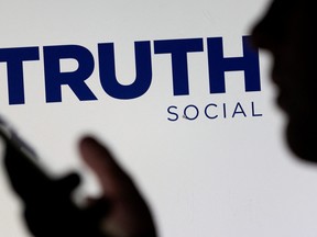 The Truth social network logo is seen displayed behind a woman holding a smartphone in this picture illustration taken Feb. 21, 2022.