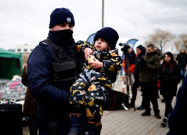 A Polish police officer carries a child to a bus, after fleeing the Russian invasion of Ukraine, at the border checkpoint in Medyka, Poland, Saturday, March 5, 2022.