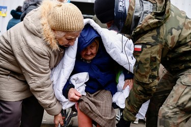 A Polish armed forces member and a woman help another woman sit in a wheelchair as she arrives at a temporary accommodation centre, after fleeing the Russian invasion of Ukraine, in Korczowa, Poland, Sunday, March 6, 2022.