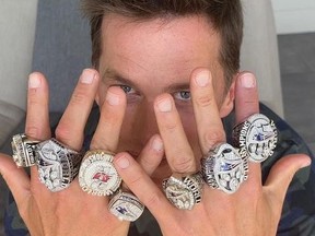 Tom Brady covering his face with his hands wearing his seven Super Bowl rings.