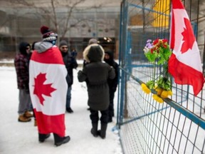 A group of people gathered at a perimeter fence along Bank St. in Ottawa, as police evicted the last of the trucks and supporters occupying the downtown core on Feb. 20, 2022.