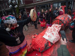 People gather around the Gassy Jack statue after it was toppled and covered in red paint during the annual Women's Memorial March, in Vancouver, on Monday, February 14, 2022.