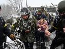 Ukrainian soldiers help an elderly woman cross a destroyed bridge as she evacuates the town of Irpin, northwest of kyiv, on March 8, 2022.