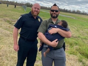 Two members of search-and-rescue team, one holding missing baby who was found alive after spending night in open field.