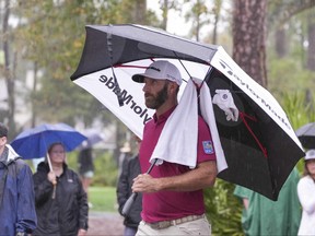 Dustin Johnson shields himself from the rain during the first round of THE PLAYERS Championship golf tournament.